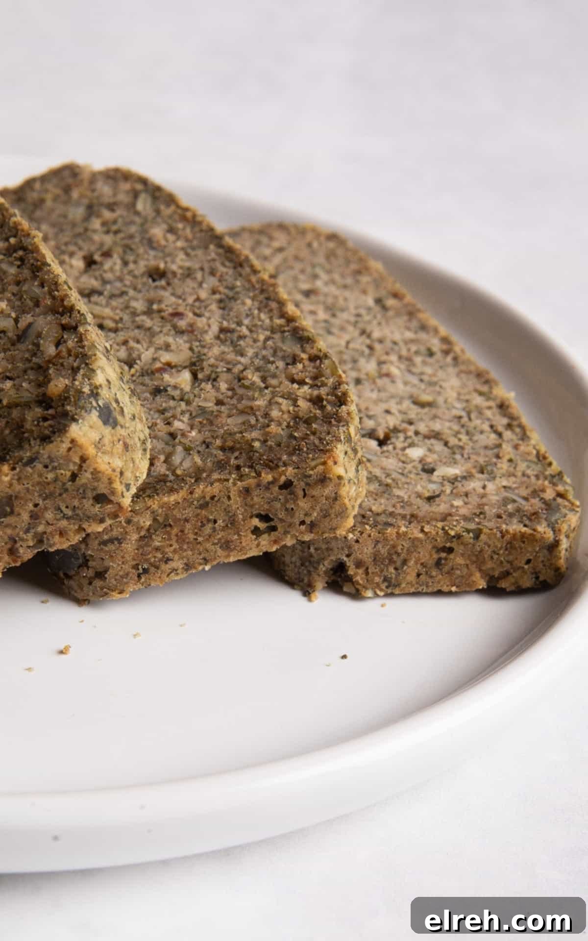Gluten-Free Seeded Loaf Recipe with Flax, Sunflower and Chia 9 sliced seeded bread on white plate on white surface.