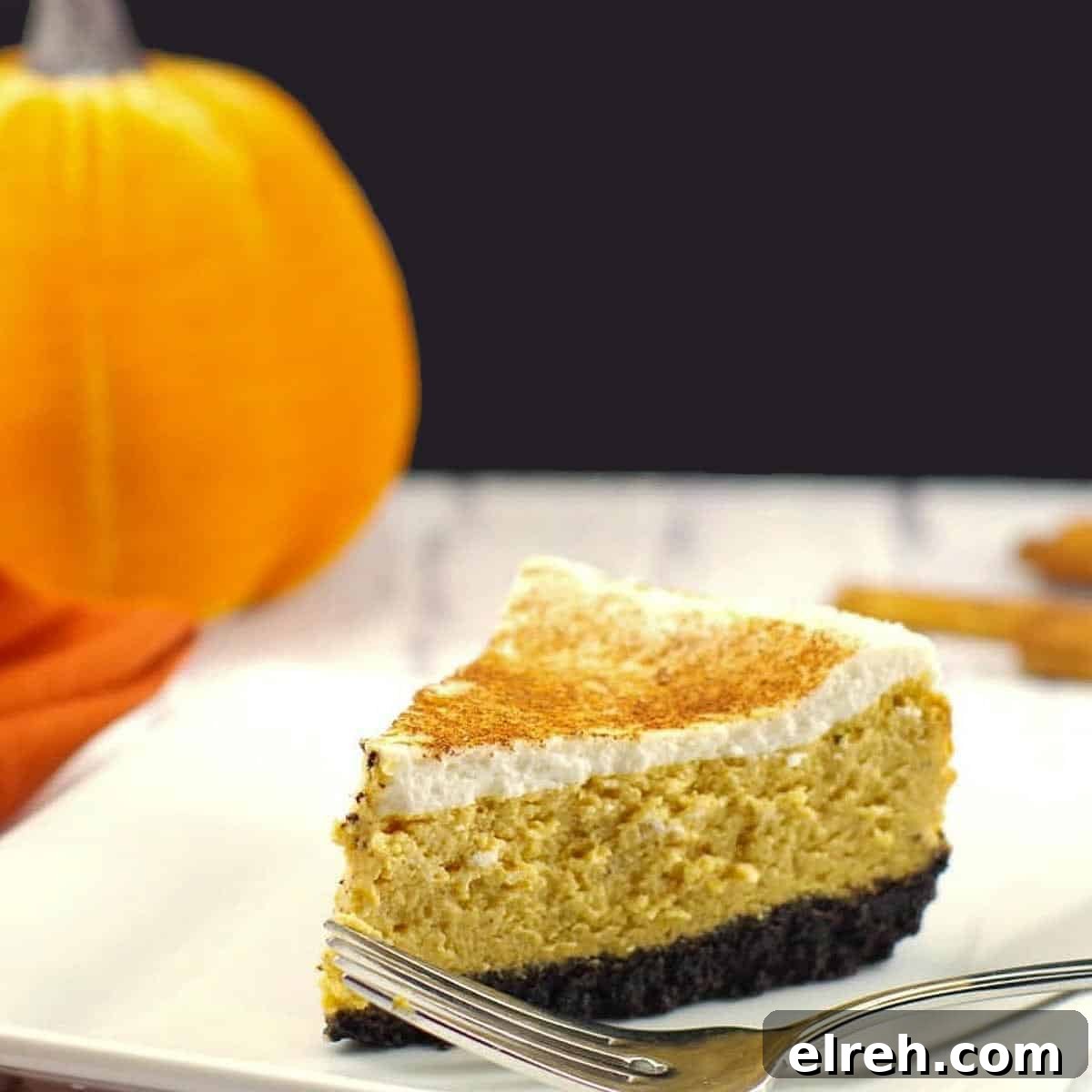 a piece of skinny pumpkin cheesecake on a white plate with fork and a stuffed pumpkin in background