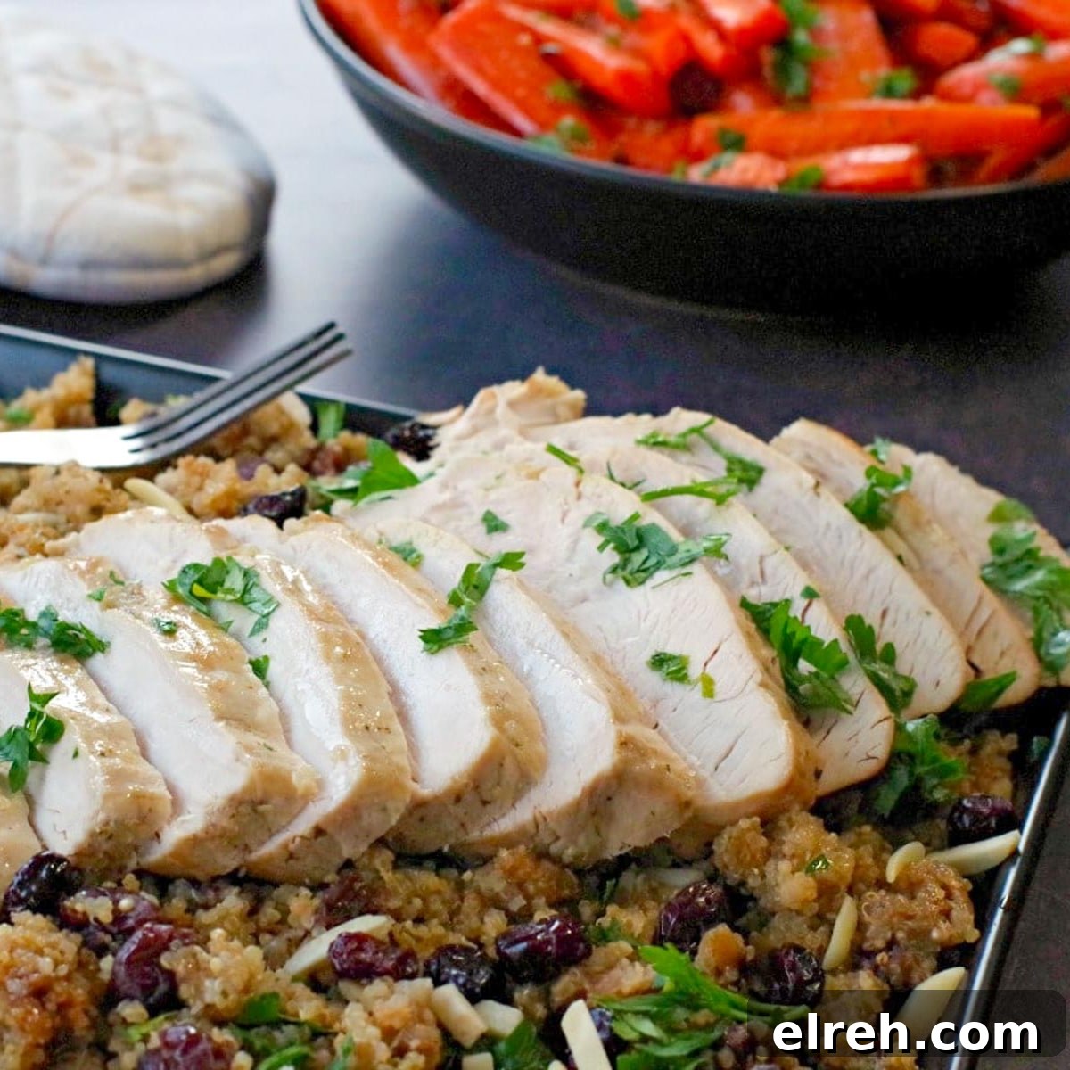 sliced slow cooker turkey breast on bed of cranberry quinoa dressing (on black platter) with black bowl of roasted carrots and festive oven mitts in the background