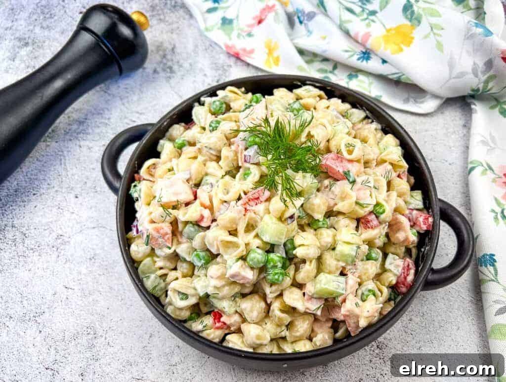 A bowl of salmon pasta salad with a creamy dressing, garnished with a sprig of dill.