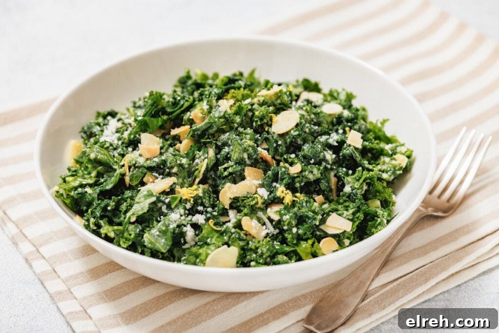 A white bowl of kale salad with lemon sits on a striped placemat beside a fork.