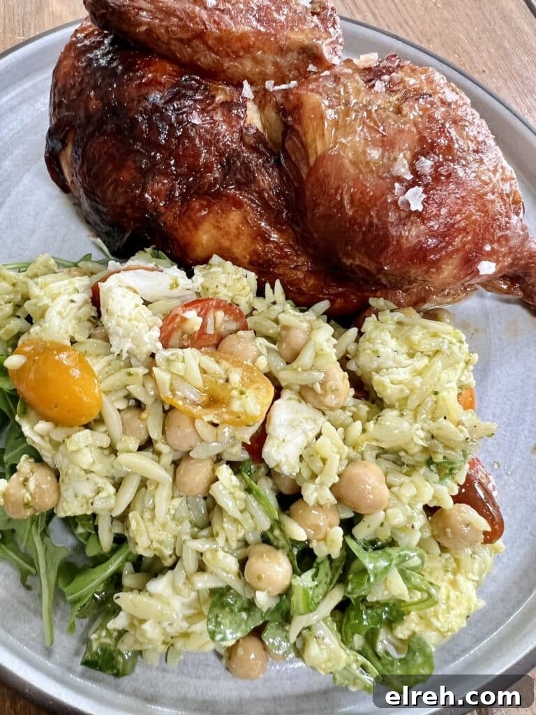 Pesto orzo pasta salad caprese on plate with roasted half chicken.
