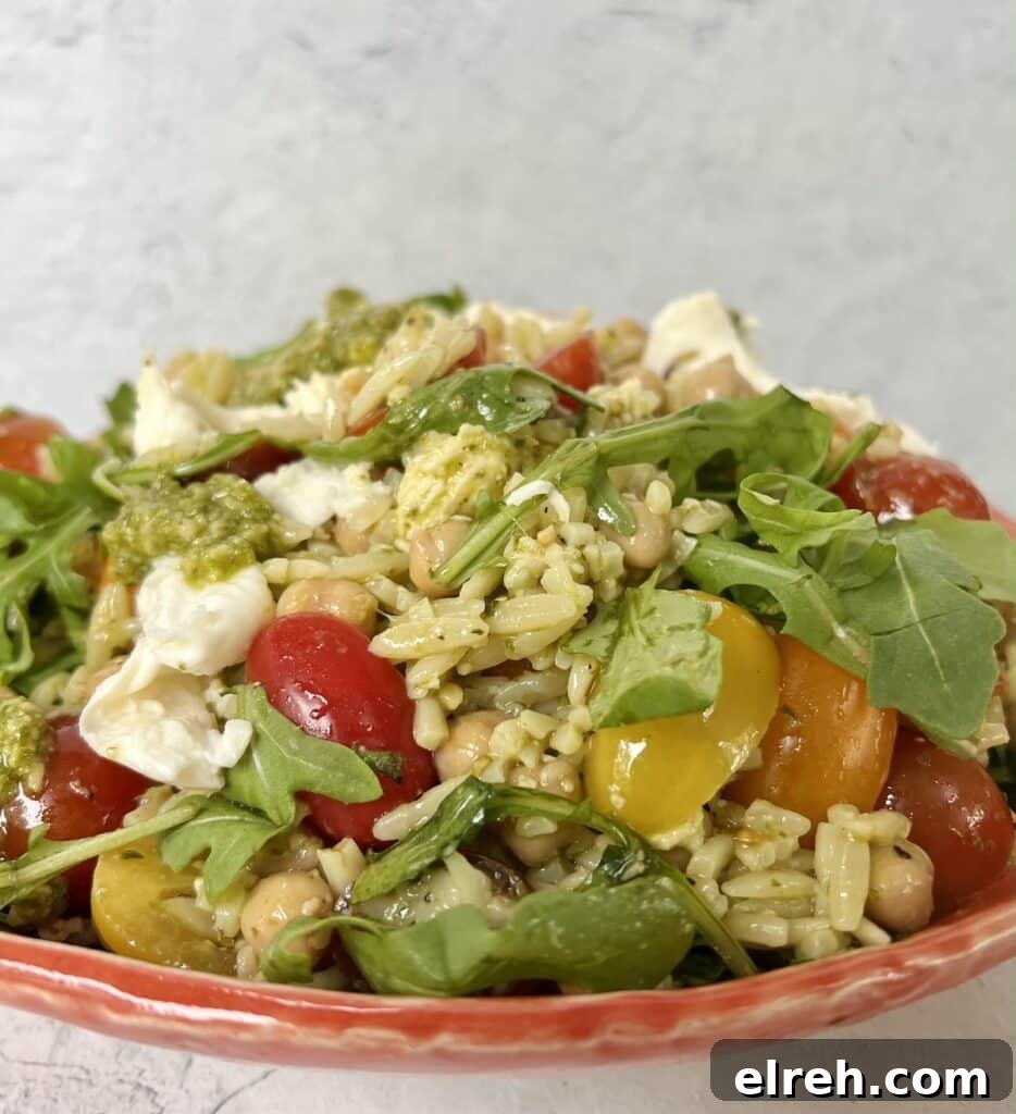 Side view of pesto orzo salad caprese in orange bowl.