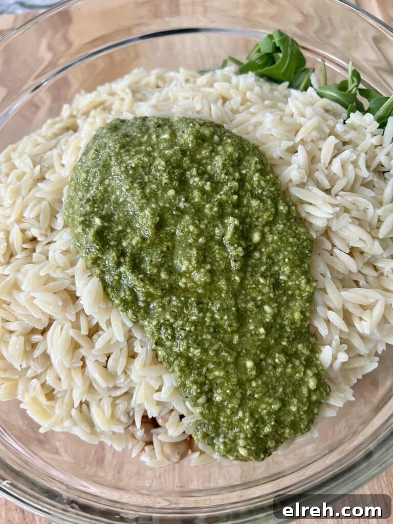 Basil pesto poured over cooked orzo about to be mixed in.