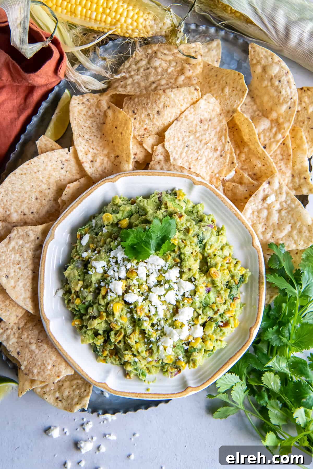 Charred Corn Guacamole Recipe with Lime and Cilantro 2 A top down shot of a bowl of corn guacamole surrounded by tortilla chips and sweet corn.
