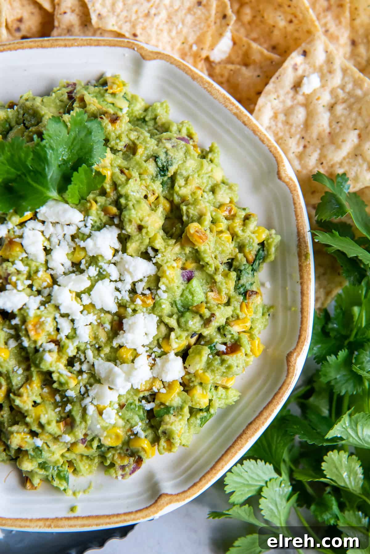 Charred Corn Guacamole Recipe with Lime and Cilantro 3 A top down shot of guacamole with corn and cotija cheese in a bowl with cilantro.