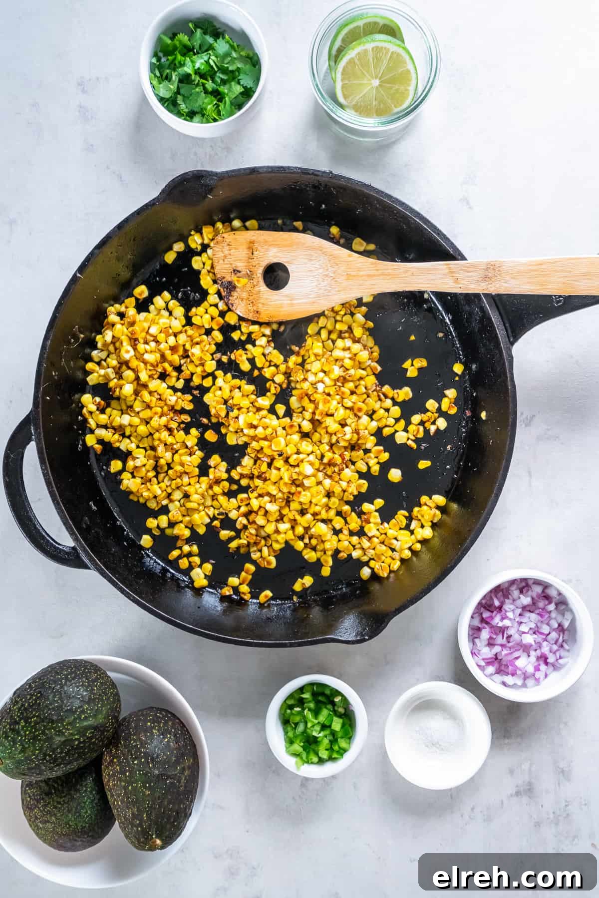 Charred Corn Guacamole Recipe with Lime and Cilantro 6 Corn in a cast iron skillet with ingredients surrounding it.
