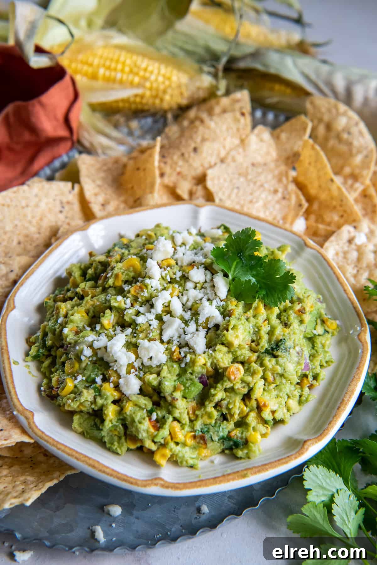 Charred Corn Guacamole Recipe with Lime and Cilantro 7 Guacamole with corn topped with cotija in a bowl surrounded by tortilla chips.