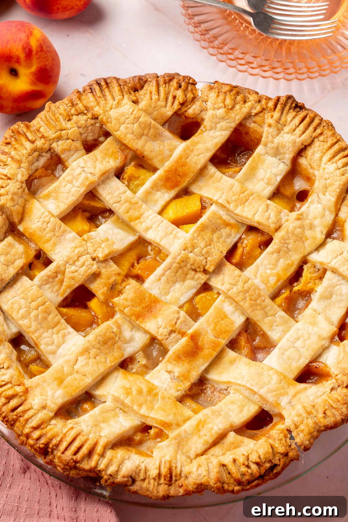 Gluten-Free Peach Mango Pie Recipe 5 A close-up of a gluten-free peach mango pie with a lattice top, with dessert plates and forks in the background.