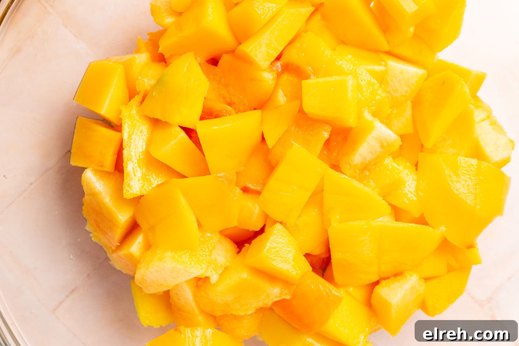 Gluten-Free Peach Mango Pie Recipe 6 A glass mixing bowl with diced peaches and mangoes in it.