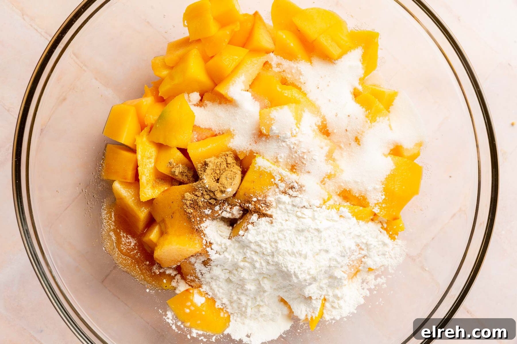 Gluten-Free Peach Mango Pie Recipe 7 A glass mixing bowl filled with diced peaches, diced mangoes, sugar, cornstarch, cinnamon, vanilla, nutmeg, and ginger before mixing.
