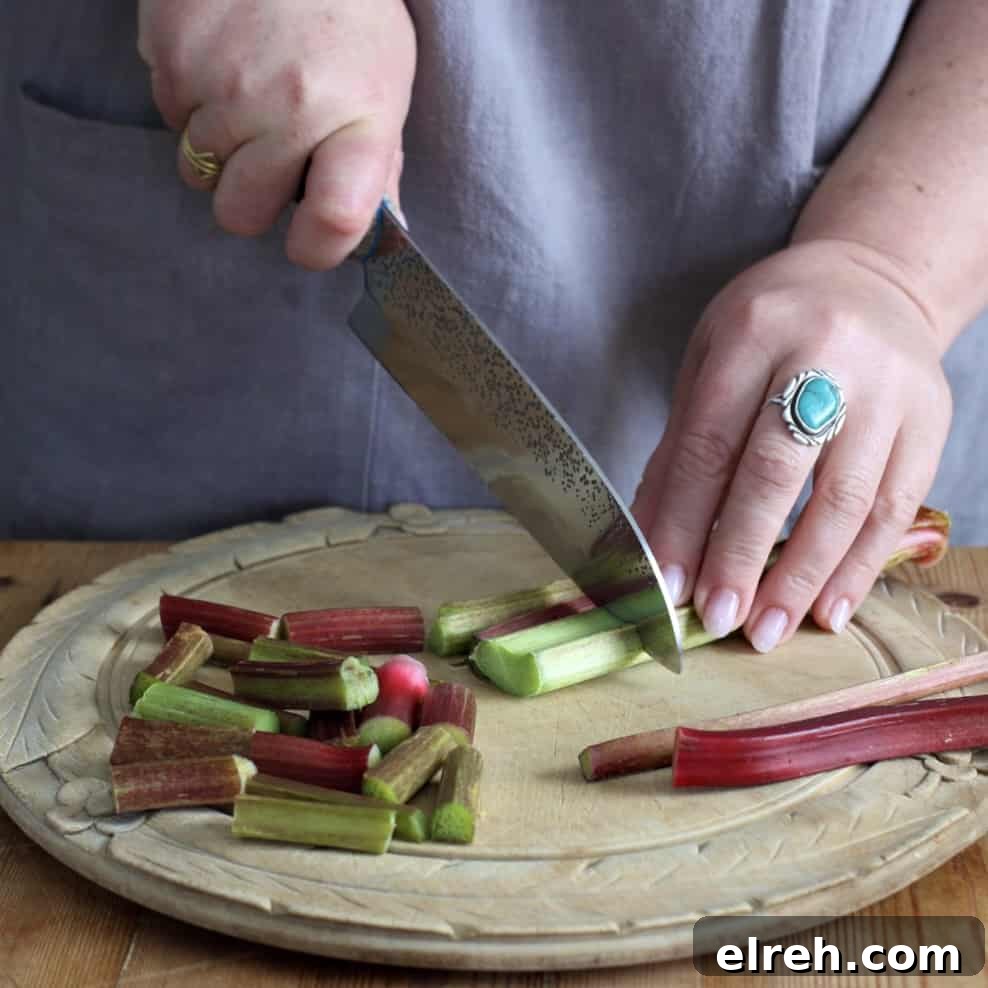 Womans hands chopping rhubarb stalks on a wooden board with a large silver knife