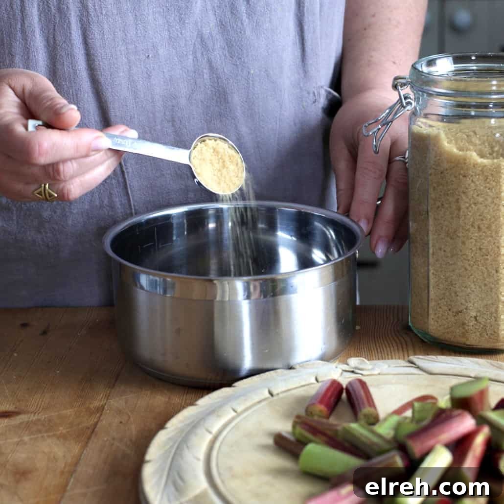 Woman tipping brown sugar from a silver measuring spoon into a small silver saucepan