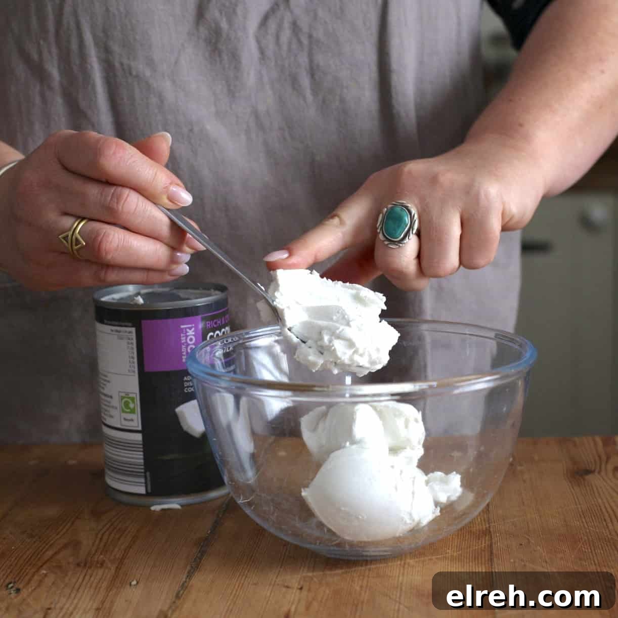 Woman scraping solid coconut cream from a black can into a glass bowl with a silver spoon