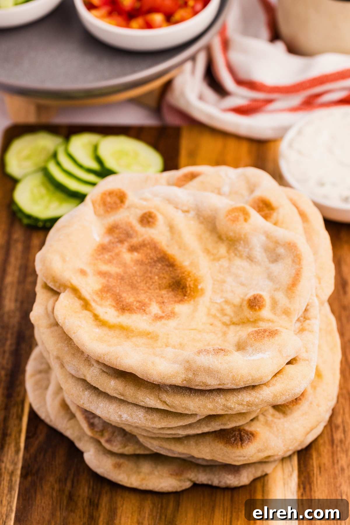 stack of pita breads with sliced cucumbers behind.