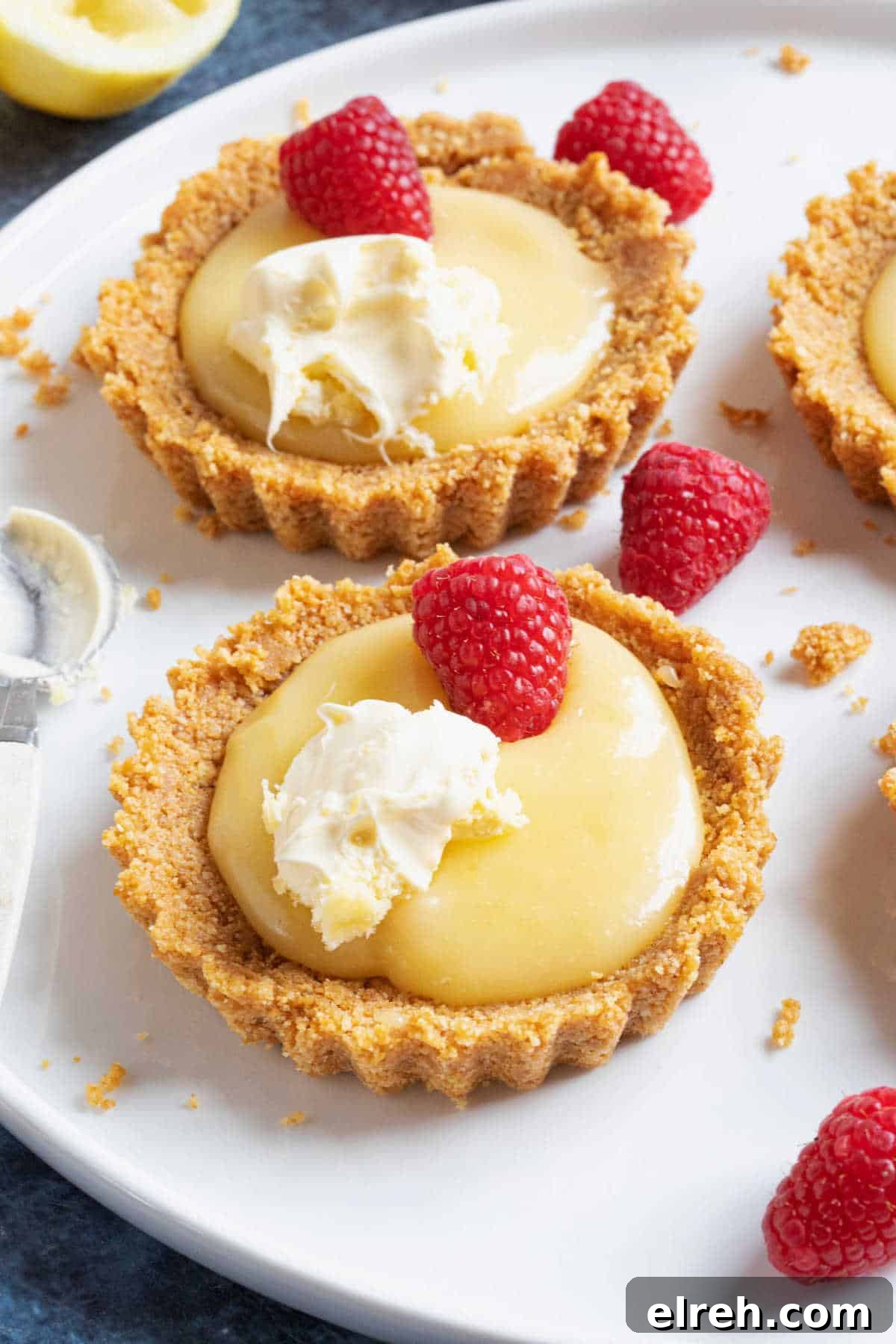 Mini Lemon Curd Tartlets with Buttery Crust 2 Mini lemon curd tartlets with a biscuit base, topped with raspberries and cream.