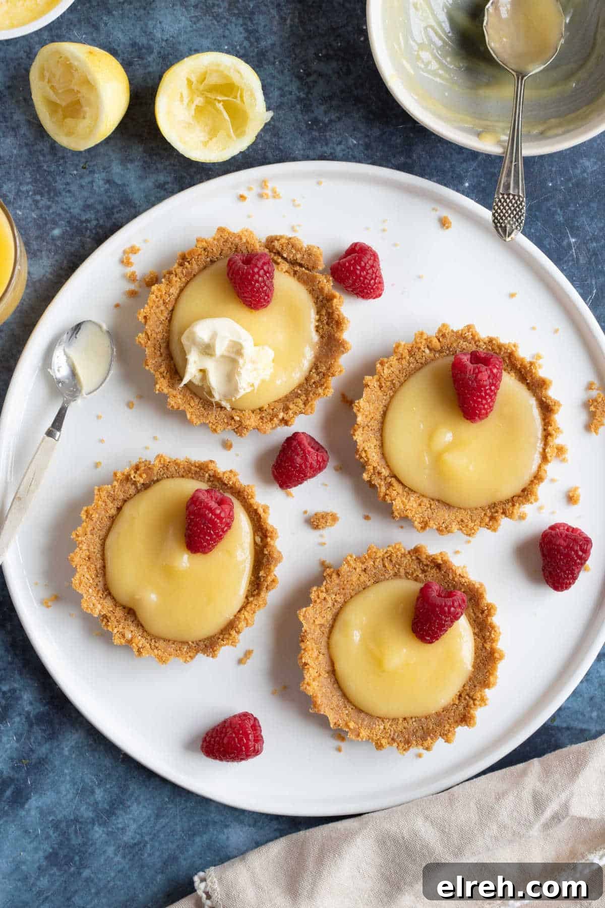 Mini Lemon Curd Tartlets with Buttery Crust 5 No bake lemon curd tartlets with a biscuit base on a white serving platter.