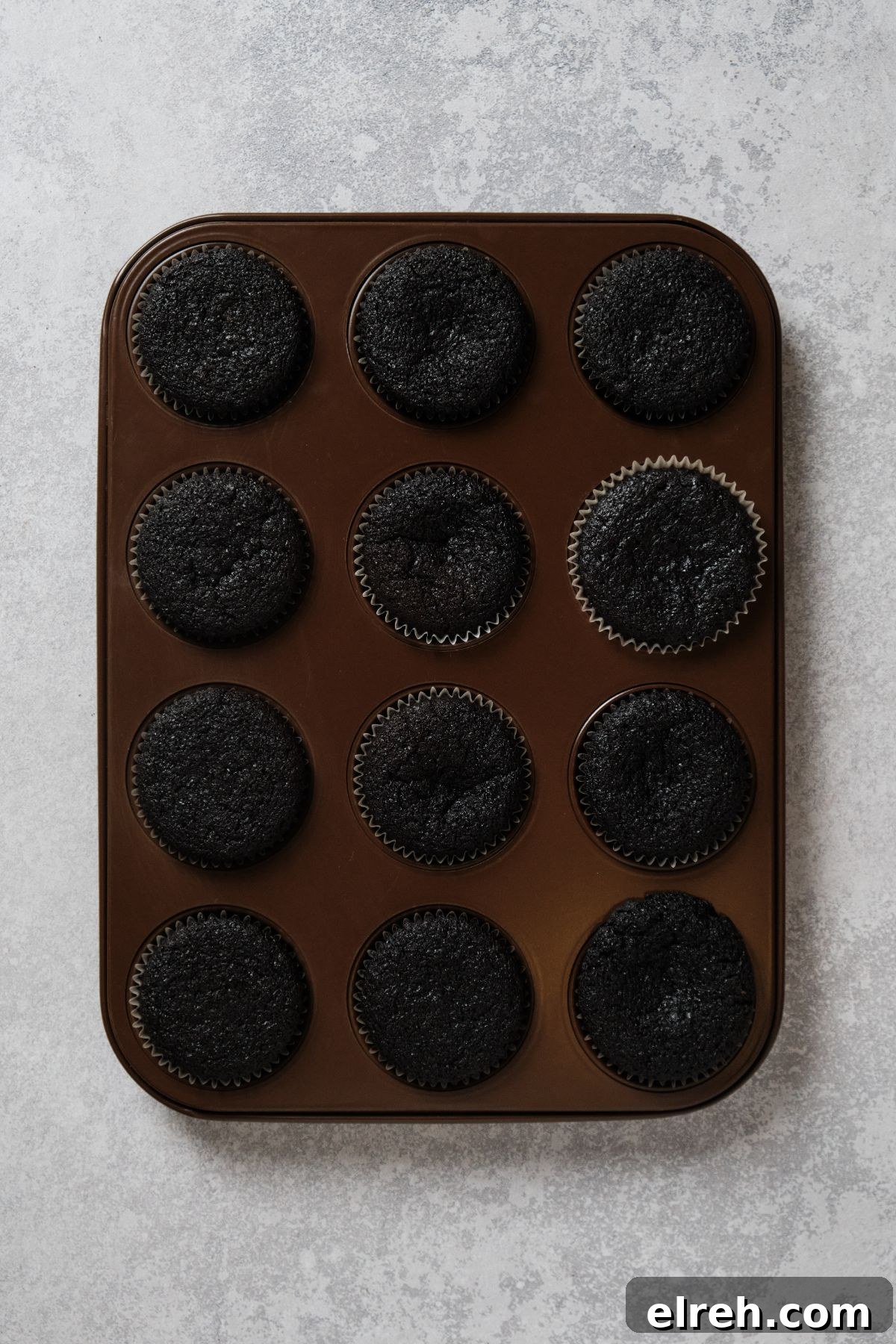 Baked chocolate cupcakes in a cupcake tin, ready to be filled with caramel.